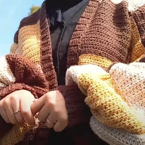 May include: A brown, beige, and yellow striped crocheted cardigan with a long sleeve and a button closure.