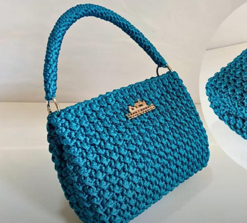 Puede incluir: Un bolso de mano de crochet azul turquesa con un cierre de metal dorado. El bolso tiene una sola correa y un dise&ntilde;o texturizado.