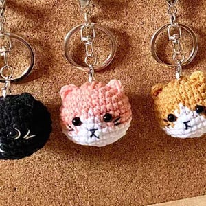 Peut inclure: Trois porte-clés en crochet en forme de chat avec du fil noir, rose et orange. Chaque porte-clés a un anneau de clé argenté.