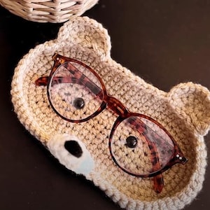Peut inclure: Un porte-lunettes en forme d'ours en crochet beige avec une paire de lunettes brunes à l'intérieur.