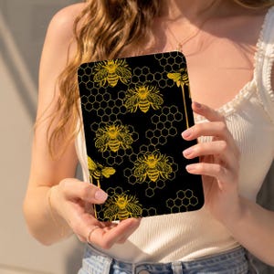 May include: A rectangular tablet case featuring a black background with a repeating gold honeycomb pattern and detailed illustrations of honeybees. The design includes multiple bees in various orientations across the surface of the protective cover.