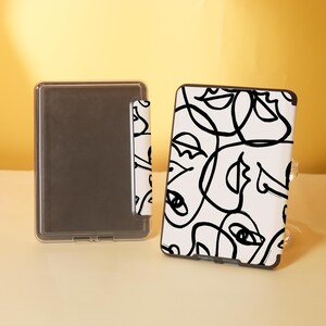 May include: A white e-reader case with a black and white abstract design of faces. The case has a clear plastic cover over the screen.