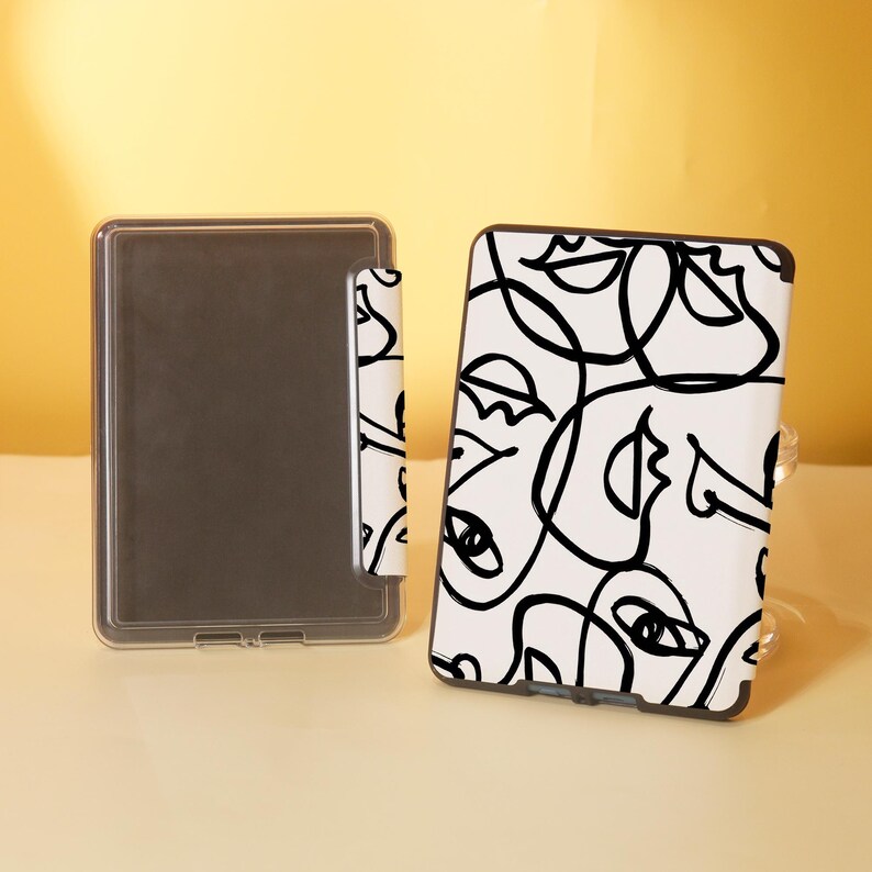 May include: A white e-reader case with a black and white abstract design of faces. The case has a clear plastic cover over the screen.