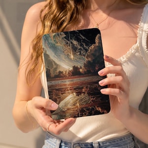 May include: A rectangular tablet case featuring a vibrant artistic print of a celestial scene with a glowing comet streaking across a dark, swirling sky above a calm, reflective body of water with deep orange, gold, and dark blue color tones.
