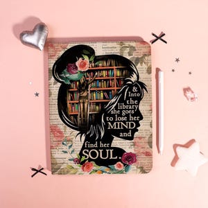 May include: A decorative notebook with a floral and book-themed design. The cover features a silhouette of a woman with the text "& Into the library she goes to lose her mind and find her soul."