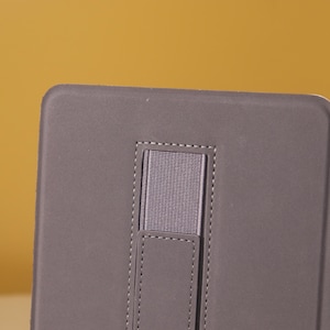 May include: A gray tablet case with a built-in elastic hand strap. The strap is sewn into the case and has a textured surface.