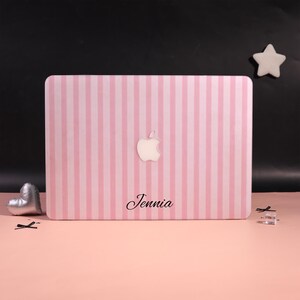 May include: A pink and white striped laptop case featuring an Apple logo and the name "Jennia". The case is set against a pink backdrop, with a silver heart and a white star in the background.