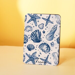 May include: A rectangular item with a white background and a blue seashell and starfish pattern. The design includes various marine illustrations and the name "Bennier". The item has a dark brown border. The design is reminiscent of coastal themes.