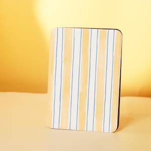May include: A rectangular coaster with a yellow and blue striped pattern. The coaster has a white background and is made of a hard material.