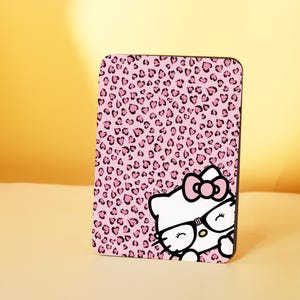 May include: Pink and black phone case with a pink leopard print background and a cartoon Hello Kitty wearing glasses. The Hello Kitty is peeking out from the right side of the case.