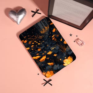 May include: A black tablet case with a floral design featuring orange flowers and a dark background. The case is rectangular with rounded corners. A Kindle e-reader is visible in the background.