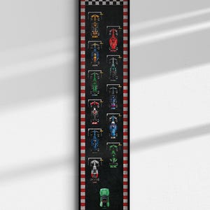 Puede incluir: Una impresión enmarcada que presenta una vista superior de coches de carreras de colores en una pista negra. La pista tiene bordes a rayas rojas y blancas y una bandera a cuadros en la parte superior. Los coches son de varios colores, incluyendo amarillo, rojo, azul y verde.