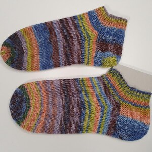 Könnte beinhalten: Ein Paar bunte gestrickte Knöchelsocken. Die Socken haben ein gestreiftes Muster mit Farbtönen von Blau, Lila, Grün, Orange und Braun. Die Socken sind aus weichem, strukturiertem Garn gefertigt.