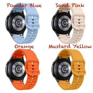 May include: Four smartwatches with coloured bands: powder blue, sand pink, orange, and mustard yellow. Each watch has a black face and a matching silicone band. The watch bands are ribbed and have a buckle closure.
