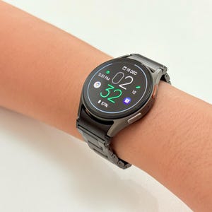 K&ouml;nnte beinhalten: Eine schwarze Smartwatch mit Metallarmband wird am Handgelenk gezeigt. Das Zifferblatt zeigt die Uhrzeit 02:32 an, zusammen mit anderen Symbolen und dem Datum 18. Dezember. Der Akkuladestand betr&auml;gt 57%.
