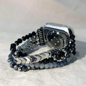May include: Silver Apple Watch with a beaded strap. The strap features black, grey, and silver beads in a layered design. The strap has a mix of round and arrow-shaped beads.