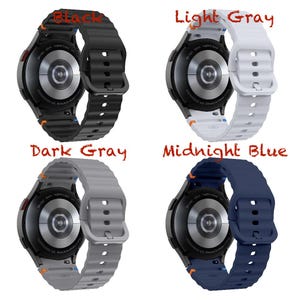 May include: Four smartwatches in black, light grey, dark grey, and midnight blue. Each watch has a round face and a silicone strap. The watch faces are black with silver detailing. The straps have a ribbed texture.