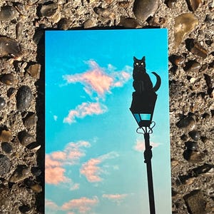 街灯の上の黒猫のポストカード - 夢のような空のイラスト - パステルカラーの雲のアートプリント - 気まぐれな猫のポストカード
