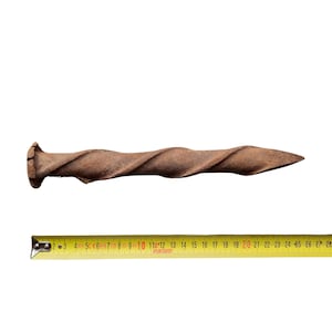 Può includere: Un chiodo di metallo contorto e arrugginito con una punta appuntita. Il chiodo è lungo circa 50 cm.