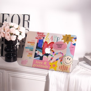 May include: A laptop computer with a pink, white and blue design. The laptop has several colourful stickers with motivational quotes, including "love your self", "happy", "you can do it", "everything is gonna be alright", "love & gratitude", and "all good things take time".