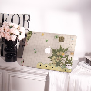 May include: A beige laptop case with a grid pattern, featuring a white Apple logo. The case is decorated with floral and cartoon graphics, including a Totoro character. The design incorporates Japanese text and decorative elements.