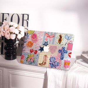 May include: A decorative laptop case featuring a patchwork design with watercolor illustrations of fruit slices, cherries, a bow, a tiger, a cross, and a cowboy boot. The case also includes the text "GOD MADE NO MISTAKE WHEN HE CREATED YOU."