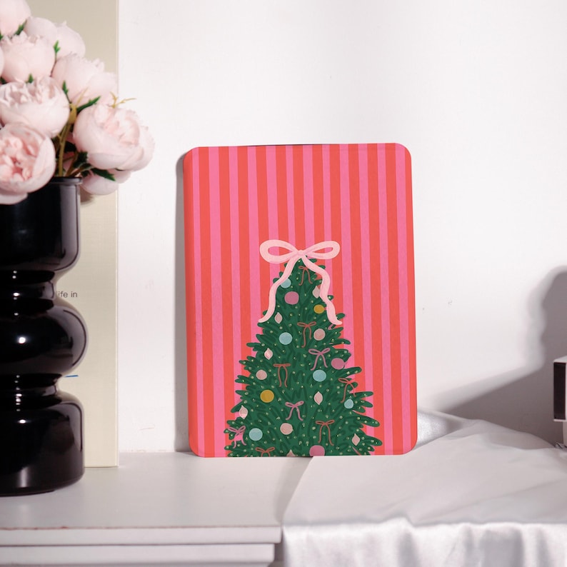 May include: A rectangular Christmas-themed card with a pink and red striped background. A green Christmas tree is decorated with colorful ornaments and pink bows. A large pink bow sits at the top of the tree.