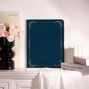 May include: A dark blue rectangular tablet case featuring a gold-colored filigree border design with ornate corner flourishes. The case has a smooth, solid-colored surface and is positioned upright, displaying a clean, symmetrical frame pattern.