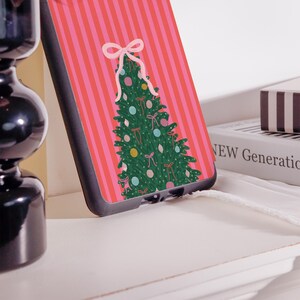 May include: A phone case featuring a Christmas tree design. The case has a pink and red striped background with a green Christmas tree decorated with bows and ornaments. The case is black.