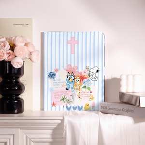 Op de afbeelding: Een lichtblauw en wit gestreepte tablethoes met een roze kruis, tekenfilmhonden, Snoopy met een ijsje, bloemen, een schelp, een gele eend en teksten zoals "cast all your anxiety on Him" en "GOD'S PLAN IS WORTH THE WAIT."