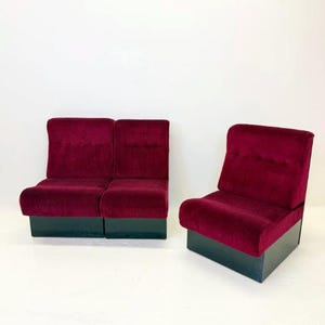 May include: Two-seater and single-seater burgundy corduroy chairs with black bases. The chairs have a rounded design and a vertical ribbed texture. The background is plain white.