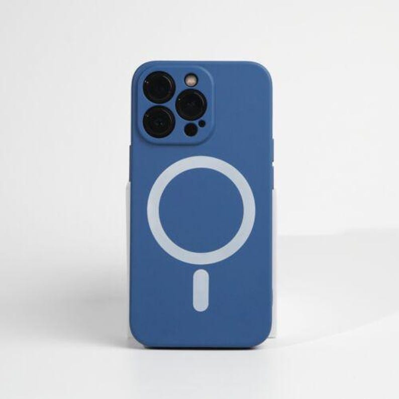 May include: A blue phone case with a white circle and a white dot in the center. The case has a raised camera bump with three black camera lenses.