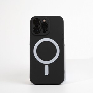 May include: Black phone case with a white ring and a white button on the back. The case has a cutout for the camera lenses.