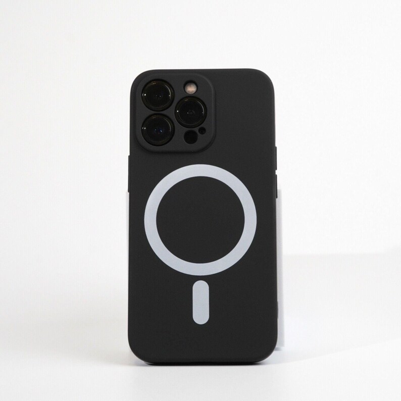 May include: Black phone case with a white ring and a white button on the back. The case has a cutout for the camera lenses.
