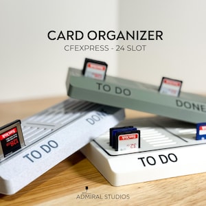 May include: A card organizer with the text "CARD ORGANIZER CFEXPRESS - 24 SLOT". The organizer is white and gray, with slots for memory cards. The words "TO DO" and "DONE" are printed on the organizer.