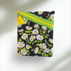 May include: Black quilted zippered pouch with a daisy print and yellow and green zipper pulls.