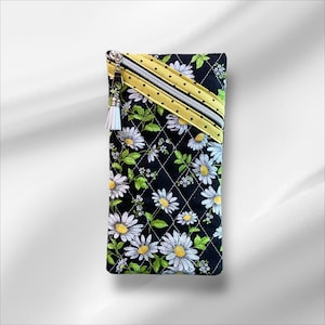 May include: A black quilted zippered pouch with a yellow and white daisy print. The pouch has a yellow zipper with black polka dots and a white tassel.