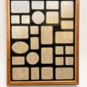 May include: A rectangular collage picture frame with a light brown wood grain finish. The frame features a black mat with multiple openings of varying shapes and sizes, including rectangles, squares, circles, and ovals. The frame measures 17.5" x 21.5".