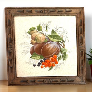 May include: A framed print featuring a still life of fruit. The artwork depicts plums, berries, and other fruit with green leaves. The frame is made of dark brown wood with carved details.