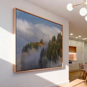 Puede incluir: Una impresi&oacute;n enmarcada de un paisaje de acantilado con un edificio en la cima, rodeado de &aacute;rboles y niebla. La obra de arte est&aacute; en un marco de madera clara, exhibida en una pared blanca. La escena evoca una sensaci&oacute;n de naturaleza y tranquilidad.