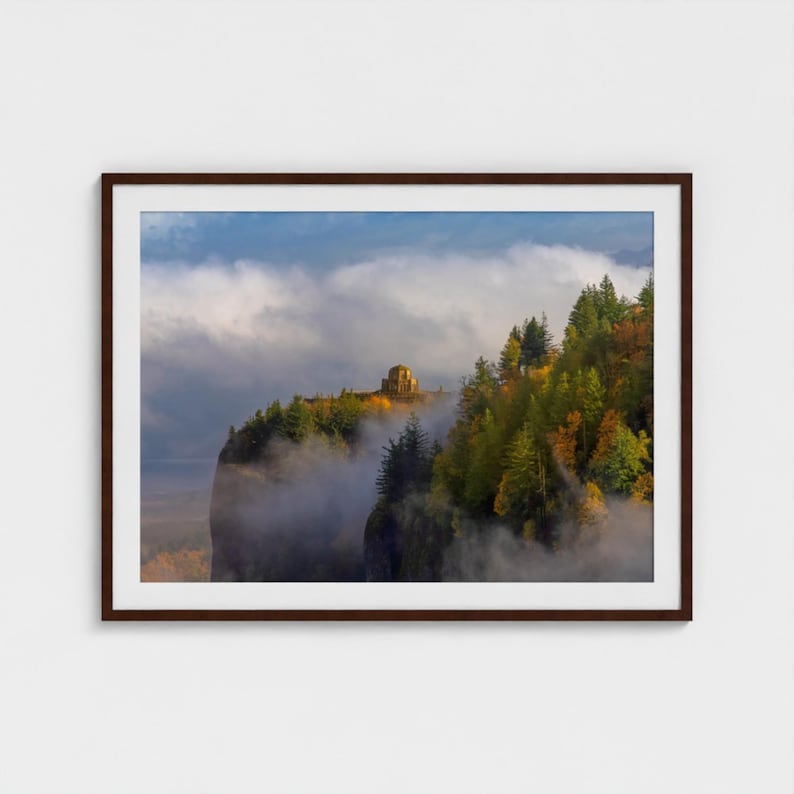 Puede incluir: Impresi&oacute;n enmarcada de un paisaje con un acantilado y una estructura de piedra en la cima de una cresta arbolada. La escena est&aacute; envuelta en niebla, con un cielo azul visible. Los &aacute;rboles muestran colores oto&ntilde;ales.