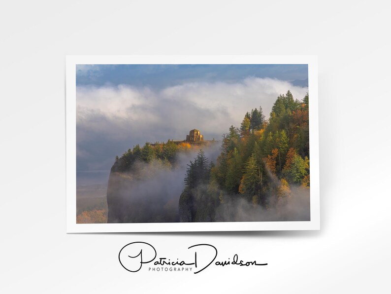 Puede incluir: Fotograf&iacute;a de un paisaje de un acantilado con una estructura en la cima, rodeado de &aacute;rboles y niebla. El cielo es una mezcla de azul y gris. Firmado "Patricia Davidson Photography".