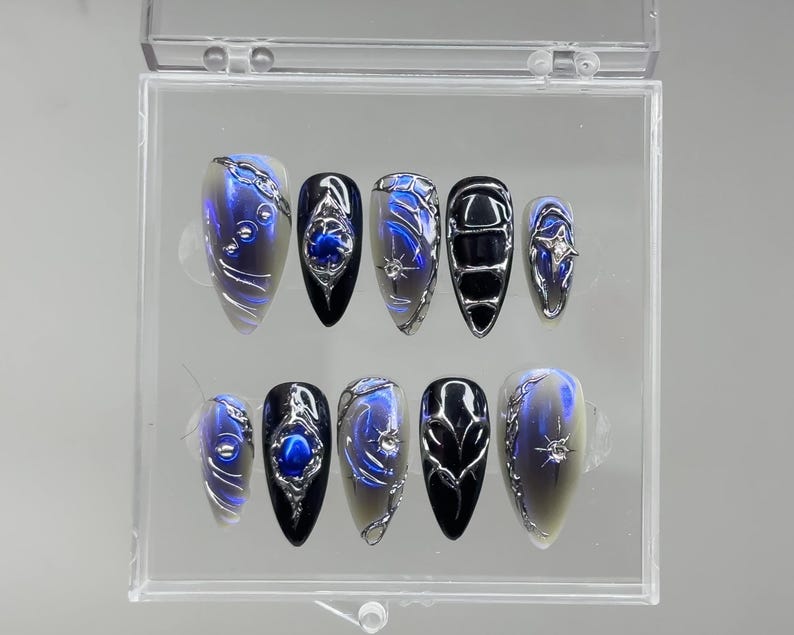 Peut inclure: Un ensemble de dix faux ongles dans un &eacute;tui en plastique transparent. Les ongles pr&eacute;sentent divers motifs, notamment des accents argent&eacute;s, des tourbillons bleus et argent&eacute;s et des bases noires et bleues. Les ongles sont de forme ovale.