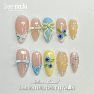 Puede incluir: Un conjunto de uñas postizas medianas en forma de almendra con varios diseños. Algunas uñas presentan una base rosa claro con motivos florales azules, otras tienen un lazo azul claro o una base amarilla con arándanos. El texto "Lemon Burberry Nails" es visible.