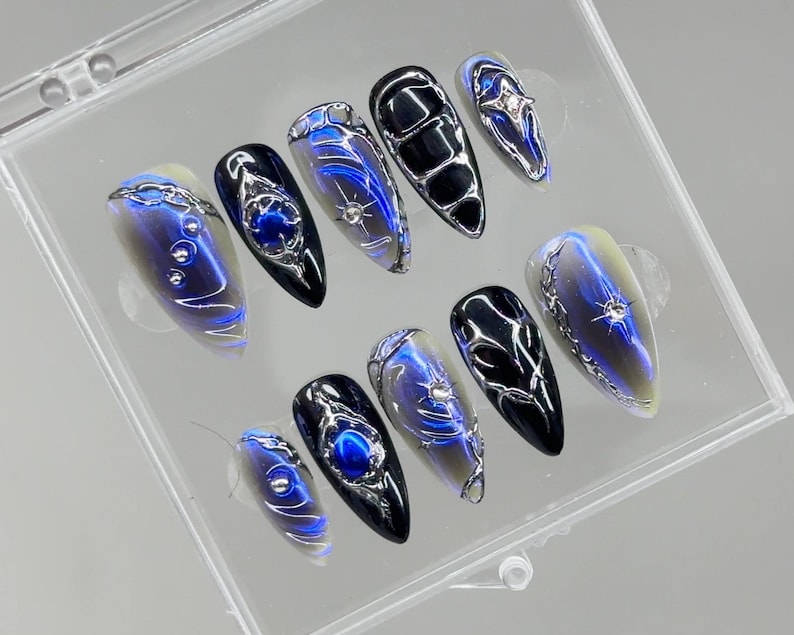Peut inclure: Un ensemble de dix faux ongles dans un &eacute;tui en plastique transparent. Les ongles pr&eacute;sentent un d&eacute;grad&eacute; de couleurs, notamment le bleu, l'argent et le noir. Chaque ongle a un design unique avec des accents m&eacute;talliques et des embellissements.
