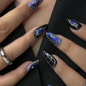 Peut inclure: Gros plan sur plusieurs faux ongles longs et pointus. Les ongles sont noirs avec des accents argent&eacute;s et bleus. Certains ongles ont un effet bleu iris&eacute;. Le texte "bae nails handmade press on nails" est visible en haut &agrave; droite.