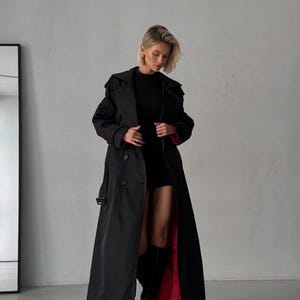 May include: A long black trench coat with a red lining. The coat has a double-breasted closure and a belt.