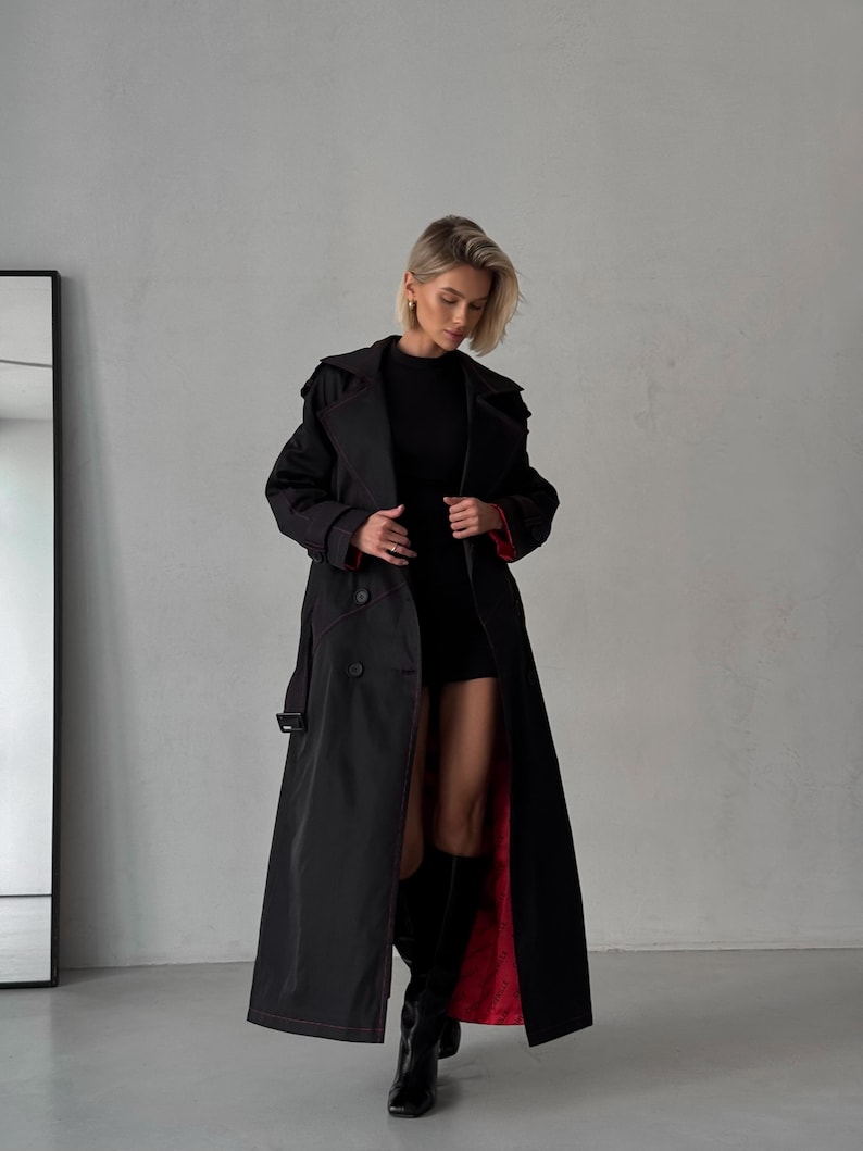 May include: A long black trench coat with a red lining. The coat has a double-breasted closure and a belt.