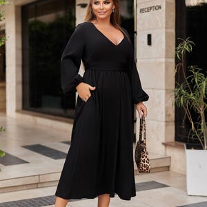 May include: A black midi dress with long sleeves and a V-neck. The dress has a fitted waist and pockets. The person is carrying a leopard print handbag and wearing leopard print heels. The word "RECEPTION" is visible in the background.