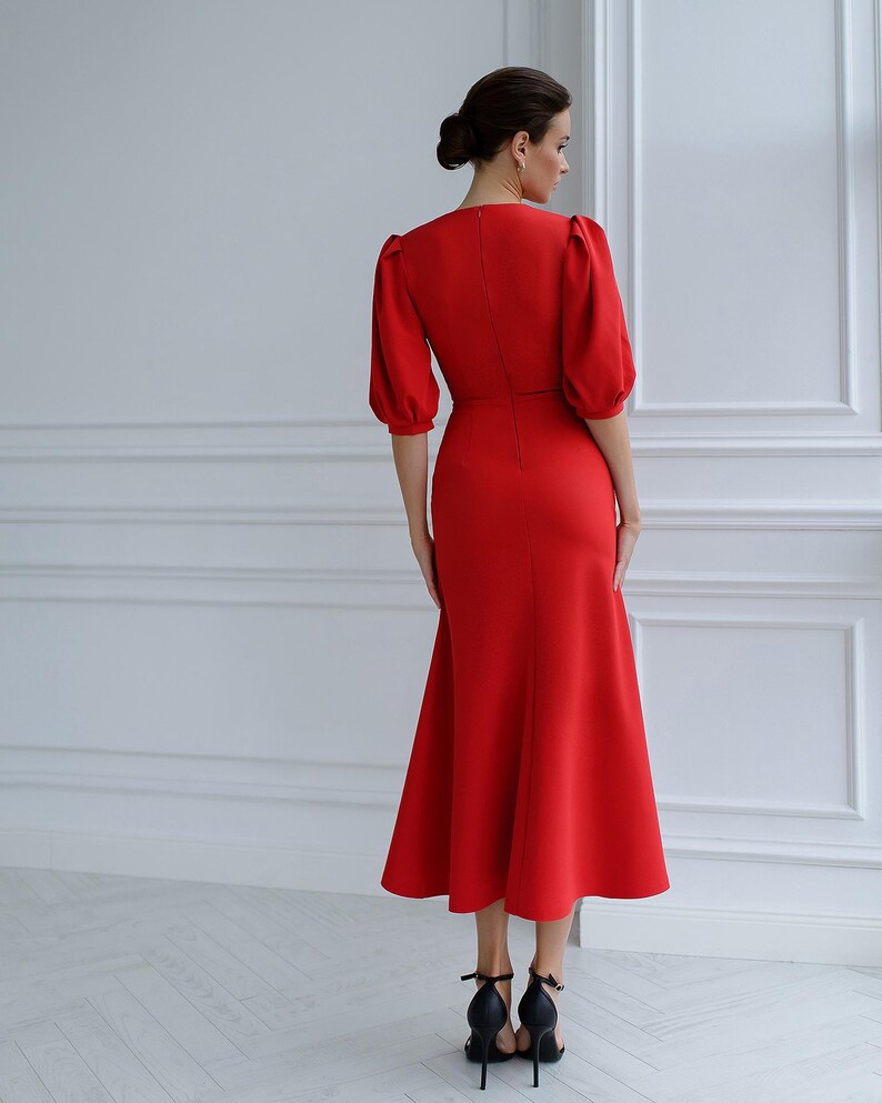 May include: A striking red dress with a fitted bodice and a flared skirt. The dress has short, puffed sleeves and a V-neck. The hemline is below the knees. The model is wearing black high-heeled sandals.